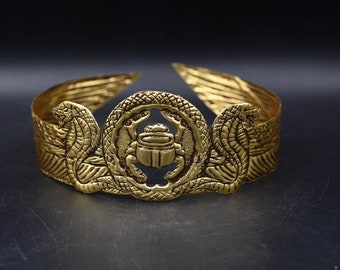 Könnte beinhalten: Goldene Krone mit einem Skarabäus-Design in der Mitte, flankiert von zwei geflügelten Schlangen.