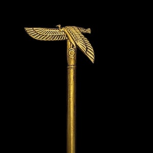 Puede incluir: Un bast&oacute;n dorado con un dise&ntilde;o de &aacute;guila en la parte superior. El &aacute;guila tiene las alas extendidas y mira hacia la derecha. El bast&oacute;n est&aacute; hecho de un metal liso y pulido.
