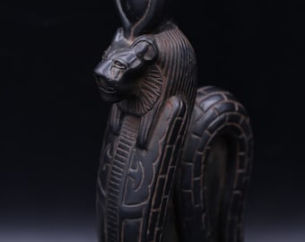May include: Black statue of the Egyptian goddess Sekhmet, depicted as a lioness with a cobra on her head. The statue is carved with intricate details and stands on a rectangular base.