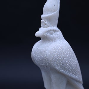 May include: White marble statue of the Egyptian god Horus, depicted as a falcon with a crown on its head.