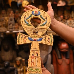 May include: A gold Ankh pendant with intricate carvings and blue and red accents. The Ankh is a symbol of life and immortality in ancient Egyptian mythology.