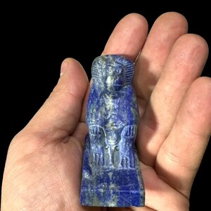 May include: A carved lapis lazuli figurine of a seated baboon. The sculpture is a deep blue color with lighter blue and gray veining. The baboon is depicted with detailed facial features and is seated on a rectangular base.