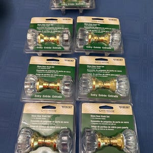 Peut inclure: Plusieurs ensembles de poignées de porte en verre. Chaque ensemble comprend deux boutons en verre transparent avec une base dorée. L'emballage porte la mention "Glass Door Knob Set" et "Entry - Entrée - Entrada".