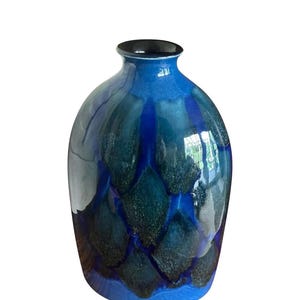 Könnte beinhalten: Eine blaue Keramikvase mit glänzendem Finish. Die Vase hat einen abgerundeten Körper und einen schmalen Hals mit schwarzem Rand. Die Oberfläche ist mit einem Muster aus dunkelblauen und teal-farbenen Formen verziert.