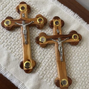 May include: Two wooden crucifixes with a silver Jesus figure. The crosses have a light brown wood grain with dark brown accents and circular insets. The crucifixes are a religious item.