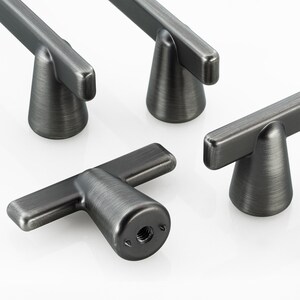 May include: A set of four T-shaped cabinet knobs with a dark brushed metal finish. Each knob features a cylindrical base that flares outward and a horizontal bar handle. One knob is positioned in the foreground, showing the threaded screw hole.
