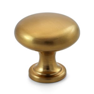 May include: A gold-colored cabinet knob with an oval top and a rounded base. The knob has a brushed metal finish and a classic design. This hardware is suitable for drawers and cabinets.