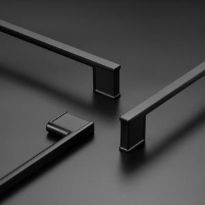 May include: Three matte black cabinet pulls with a linear, rectangular design. Each handle features a long, slender bar connected to two square-shaped mounting bases at the ends, showcasing a clean, uniform finish and a modern, geometric aesthetic.