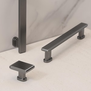 May include: A set of three dark gray metal cabinet hardware pieces featuring a brushed finish. The collection includes one vertical handle, one horizontal bar handle, and one small rectangular knob, all with rounded edges and oval-shaped bases.