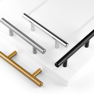 May include: Four cabinet pulls in different finishes: gold, silver, black, and brushed nickel. The pulls are all the same size and shape, with a simple, modern design.