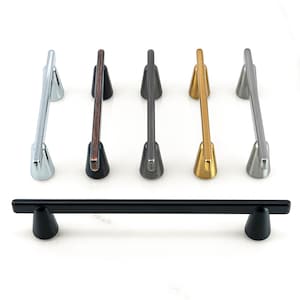May include: Five different metal cabinet pulls with a tapered design. The pulls are in silver, bronze, black, gold, and nickel finishes.
