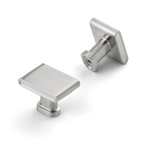 May include: Two brushed nickel cabinet knobs with a rectangular face and rounded edges. The knobs have a square base and a cylindrical post for mounting. The hardware is shown against a white background.