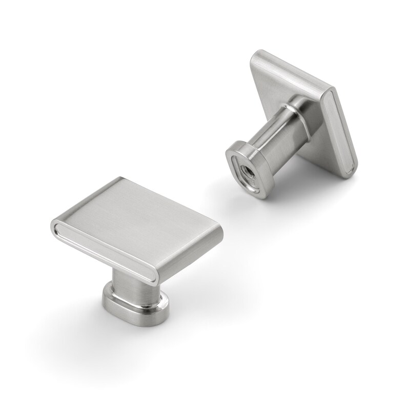 May include: Two brushed nickel cabinet knobs with a rectangular face and rounded edges. The knobs have a square base and a cylindrical post for mounting. The hardware is shown against a white background.