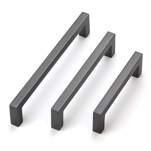 May include: Three matte black cabinet pulls arranged in a diagonal row. Each handle features a linear, rectangular bar design with two perpendicular mounting posts at the ends, showcasing a brushed metal texture across the surface of the hardware.