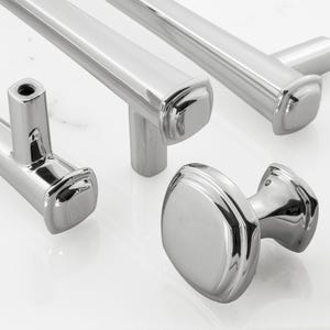 May include: A collection of polished chrome hardware including two long bar pulls with square-edged ends and one matching round cabinet knob. Each piece features a reflective metallic finish and a smooth, contoured design for cabinetry.