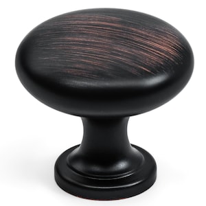 May include: A dark bronze cabinet knob with an oval shape. The knob has a smooth, rounded top with a brushed texture and a dark bronze finish. The base is a smaller, circular shape, and the stem is a simple, cylindrical design.