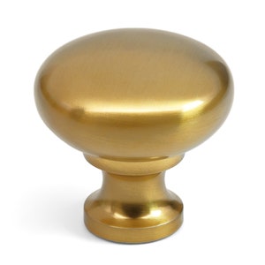 Puede incluir: Un pomo de mueble redondo con acabado en oro cepillado. El herraje presenta una superficie superior lisa y abovedada que se transforma en una base cilíndrica cónica. La superficie metálica refleja la luz, resaltando su forma circular.