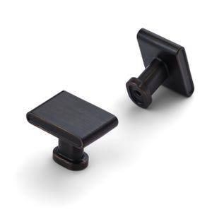 May include: Two bronze-colored cabinet knobs with a rectangular face and rounded edges. The knobs have a simple, modern design and are set against a white background. The knobs are likely for drawers or cabinets.