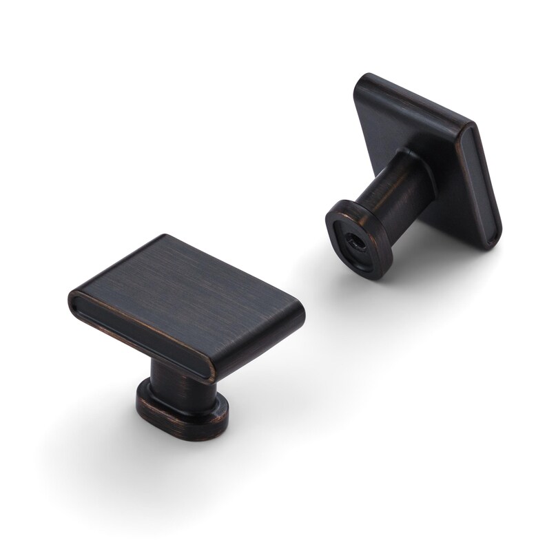 May include: Two bronze-colored cabinet knobs with a rectangular face and rounded edges. The knobs have a simple, modern design and are set against a white background. The knobs are likely for drawers or cabinets.
