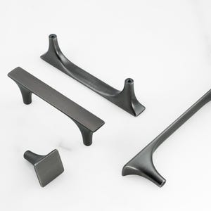 May include: A collection of four dark gray cabinet hardware pieces. The set includes two long handles, a square knob, and a curved handle. The hardware has a modern, minimalist design, suitable for drawers and cabinets.