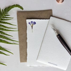 May include: A white card with a pressed purple flower and the text "naked linen" on a brown card.