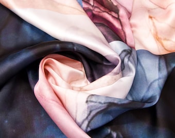 May include: A silk scarf with a pink, white, and blue abstract floral print. The scarf is folded and twisted, showing the different colors and patterns.