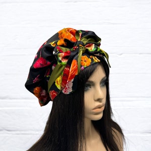 May include: A black and green floral print headscarf with a large bow tied on top. The scarf is worn on a mannequin with long black hair.