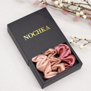 May include: Two satin scrunchies in a black box with the word "NOCHKA" printed in gold. The scrunchies are in shades of pink.