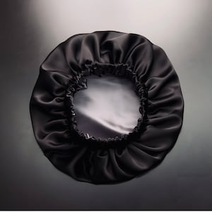 Op de afbeelding: Een zwarte satijnen slaapmuts met een gerimpeld ontwerp. De muts heeft een witte satijnen voering.