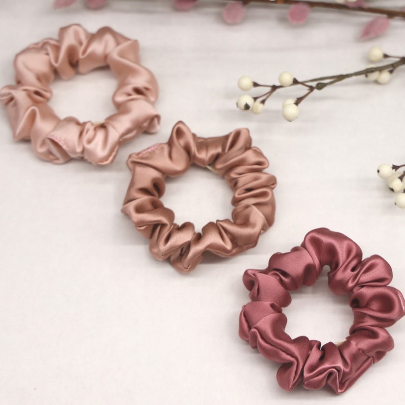 May include: Three satin scrunchies in shades of pink and brown. The scrunchies are made of soft, silky fabric and are perfect for holding hair in place.