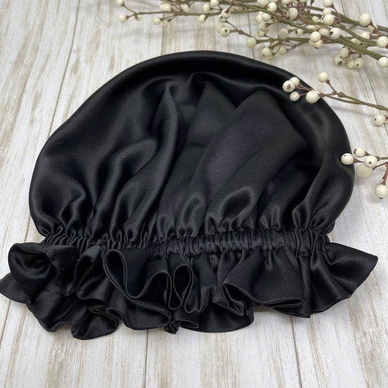 May include: A black satin sleep cap with a ruffled edge. The cap is designed to protect hair from breakage and frizz.