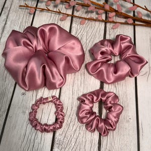 May include: Four pink satin scrunchies in different sizes. The largest scrunchie is a large, loose bun scrunchie. The other three are smaller and more compact.