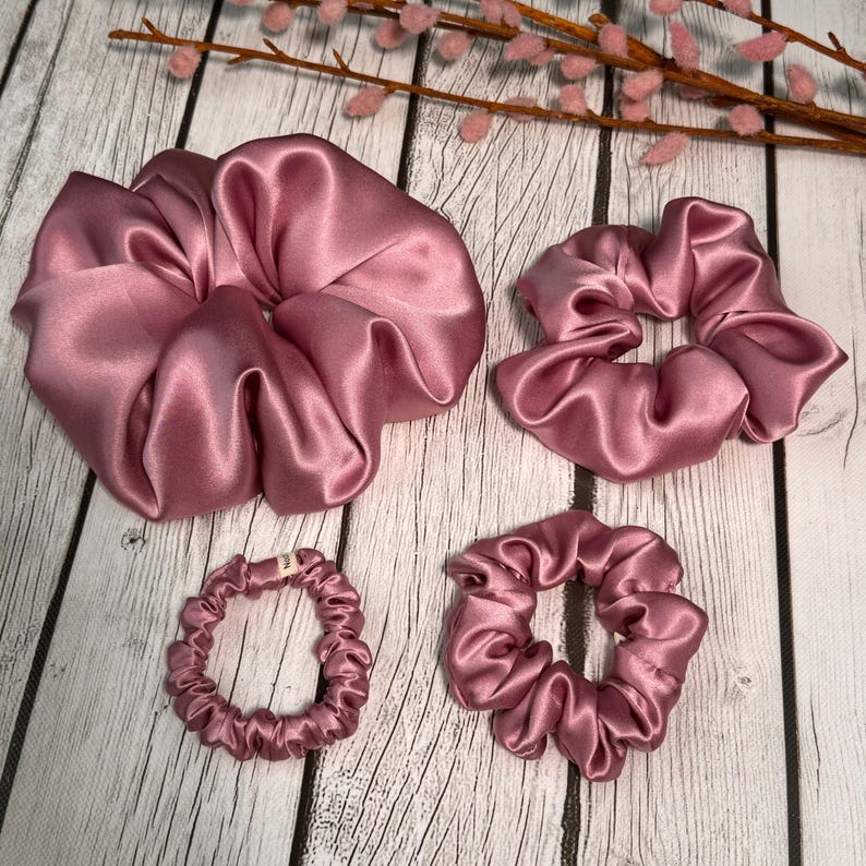 May include: Four pink satin scrunchies in different sizes. The largest scrunchie is a large, loose bun scrunchie. The other three are smaller and more compact.