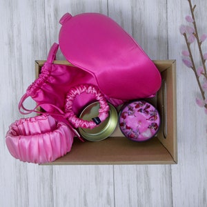 Può includere: Una maschera per dormire in raso rosa, un cerchietto in raso rosa, una maschera per dormire in raso rosa, una candela rosa con fiori secchi e un piccolo contenitore di latta in una scatola di cartone marrone.