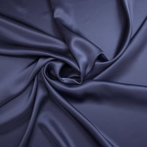 Puede incluir: Una tela de satén azul oscuro lisa con pliegues y arrugas suaves. La tela está drapeada y doblada para crear un aspecto lujoso y elegante.