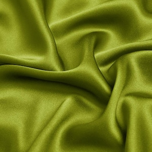 Puede incluir: Primer plano de una vibrante tela verde oliva con un brillo sedoso. El material está drapeado en suaves pliegues, creando sombras y reflejos que enfatizan su textura suave. La tela parece ser un textil lujoso, posiblemente seda o satén.