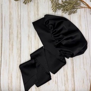 May include: A black satin sleep cap with a gathered top and a long, thin satin ribbon attached. The ribbon is tied in a knot and the ends are left loose.