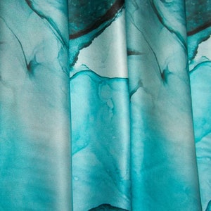 May include: Teal blue fabric with a marbled pattern. The fabric is folded and draped, showing the texture and flow of the material.