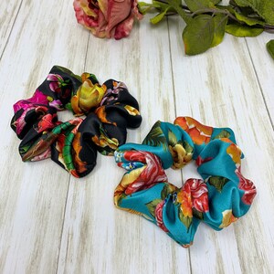 May include: Two floral print hair scrunchies. One is black with pink, yellow, and green flowers. The other is teal with orange, yellow, and pink flowers.