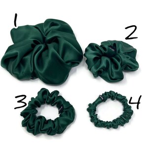 May include: Four green satin scrunchies in different sizes. The largest scrunchie is in the shape of a flower. The other three scrunchies are round.