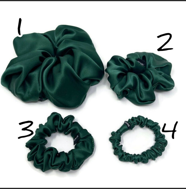 May include: Four green satin scrunchies in different sizes. The largest scrunchie is in the shape of a flower. The other three scrunchies are round.