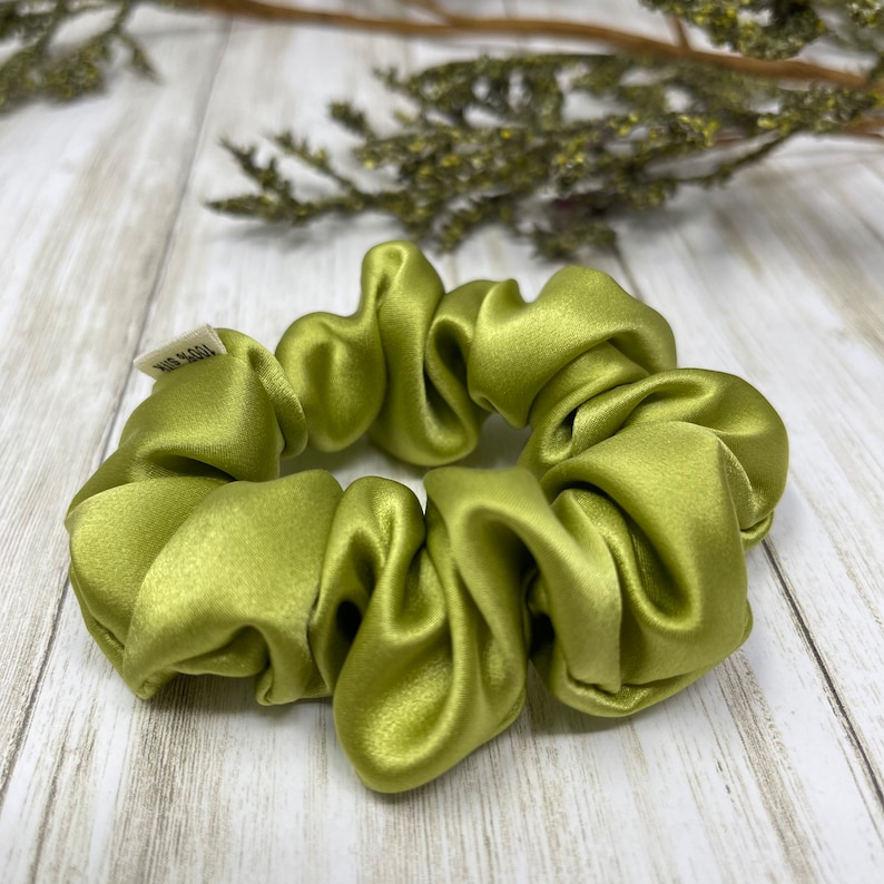 May include: A green satin scrunchie for hair. The scrunchie is made of soft, silky fabric and is designed to be gentle on hair.