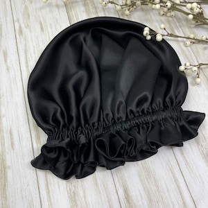 May include: Black satin sleep cap with a ruffled edge. The cap is designed to protect hair from breakage and frizz.
