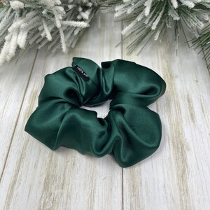 May include: A dark green satin scrunchie with a black tag that reads "100% Silk".