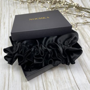 May include: A black satin sleep cap with ruffles, packaged in a black box with the word "NOCHKA" printed in gold lettering.