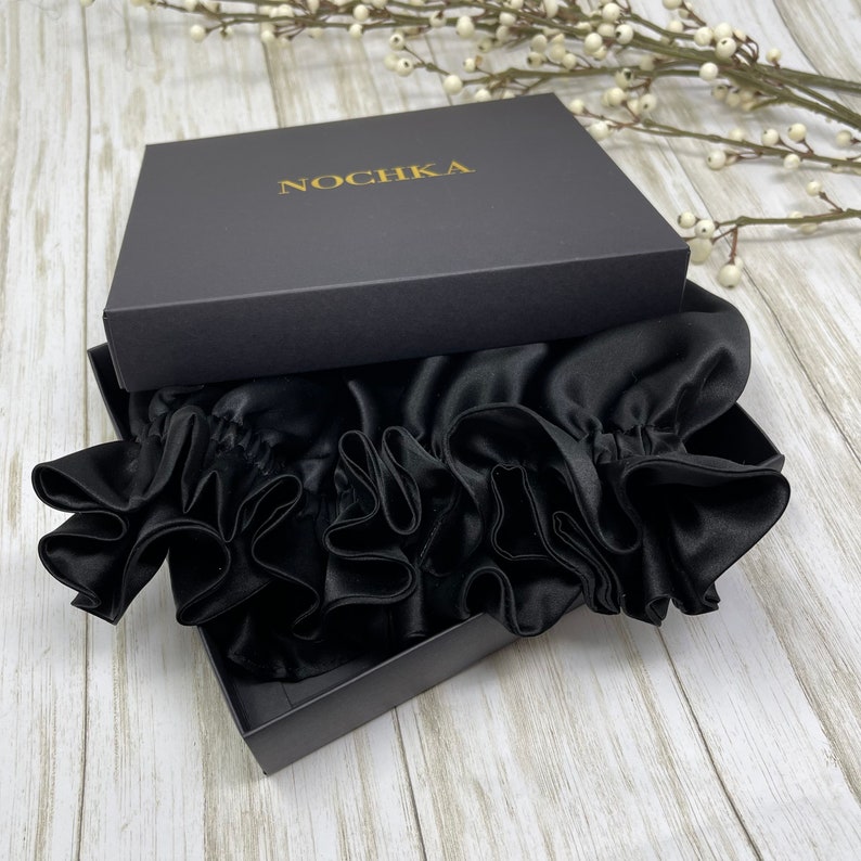 May include: A black satin sleep cap with ruffles, packaged in a black box with the word "NOCHKA" printed in gold lettering.