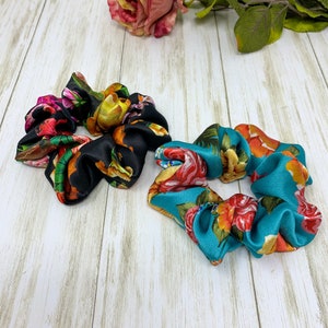 May include: Two floral print hair scrunchies. One is black with yellow, pink, and green flowers. The other is teal with orange, yellow, and pink flowers.