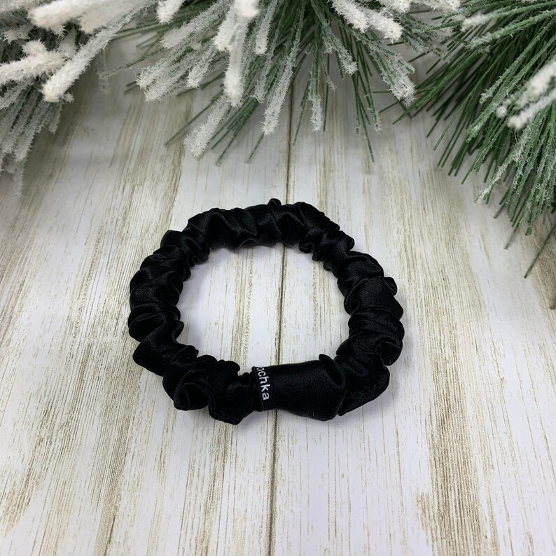 K&ouml;nnte beinhalten: Ein schwarzes Seidenhaarband mit dem Wort "Scrunchie" darauf.
