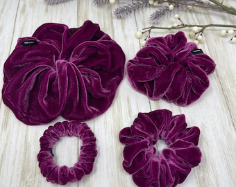 May include: Four purple velvet scrunchies of different sizes. The largest scrunchie is folded in half and the smallest scrunchie is about the size of a quarter.