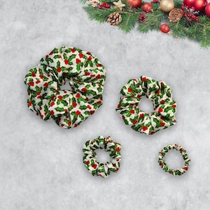 May include: Three different sizes of hair scrunchies with a holly and berry pattern. The scrunchies are white with green holly leaves and red berries.